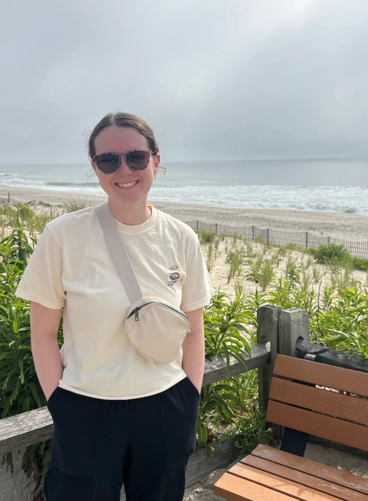 Olivia Laughman, Website Designer for Private Practices posing by the ocean wearing sunglasses and a cream fanny pack