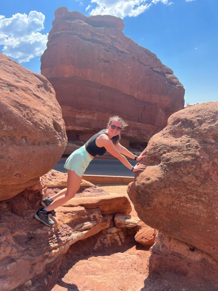 Weight-inclusive website designer, Olivia Laughman, posing with red rocks on a hiking trail in Colorado Springs