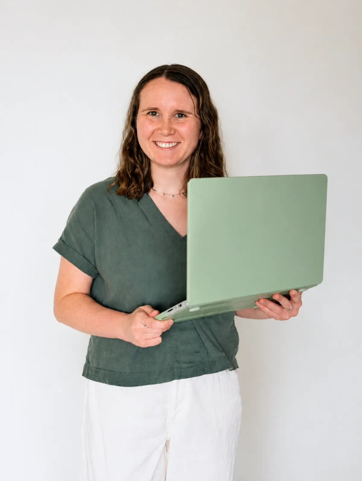 A professional photo of Website Designer and Dietitian Olivia Laughman wearing a green shirt, holding her laptop