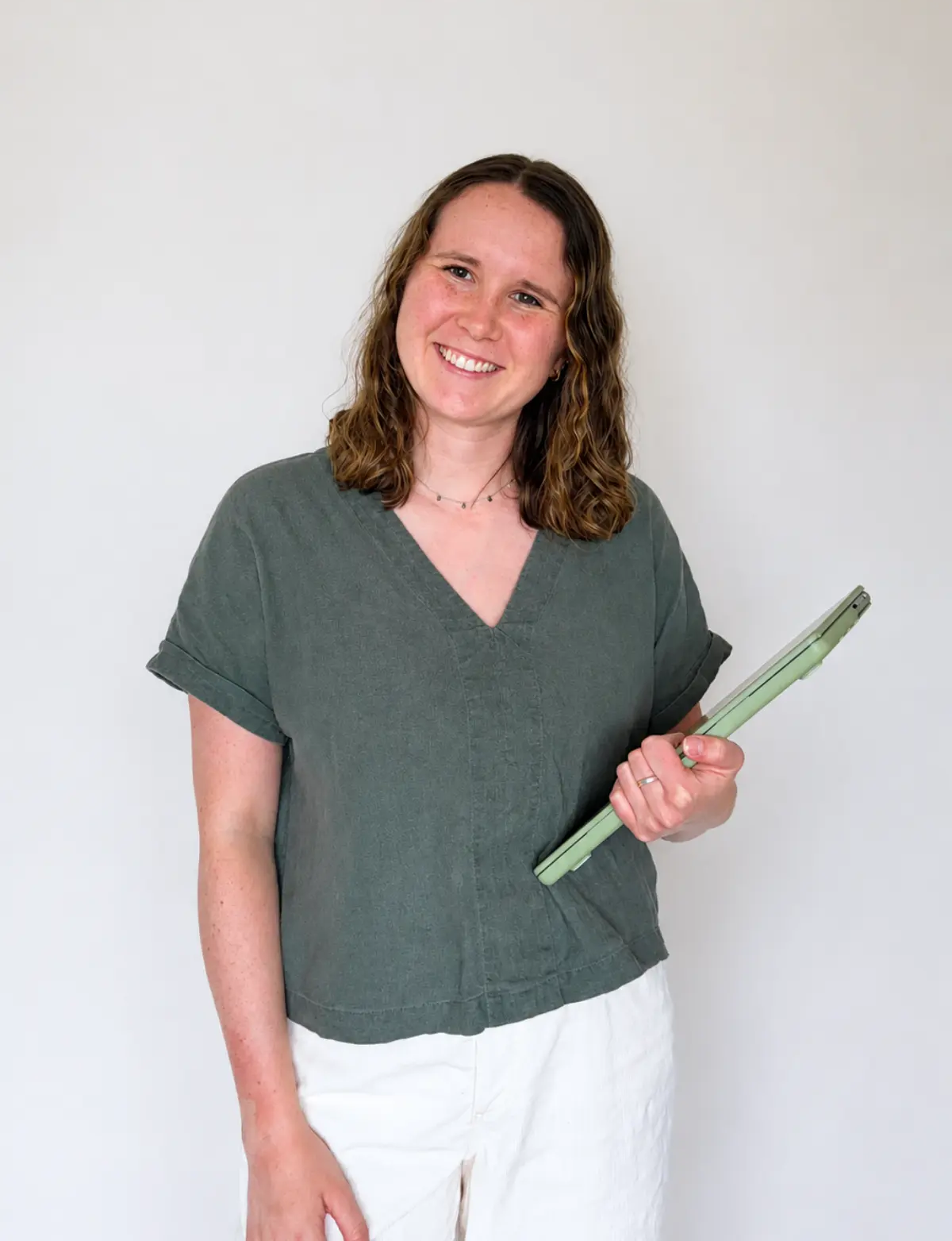 Headshot of website designer, Olivia Laughman RDN, holding her closed laptop in a green shirt