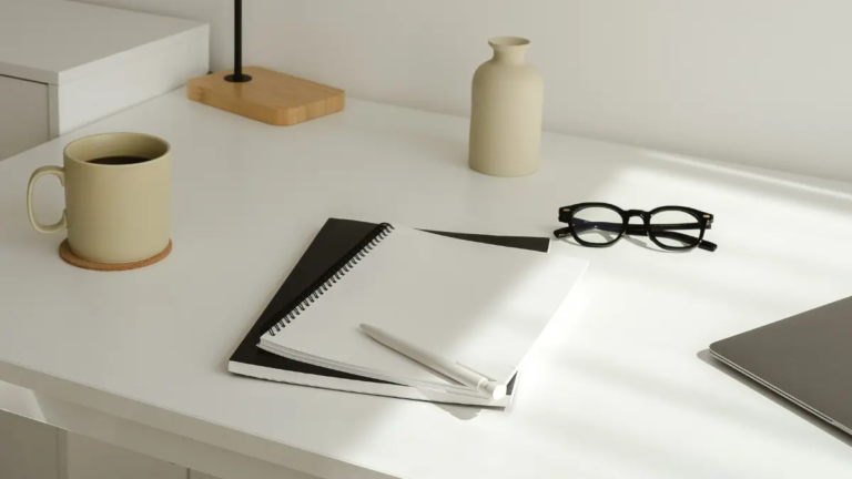 A white desk with glasses, a coffee mug, and a notebook for writing down the differences between Squarespace and WordPress