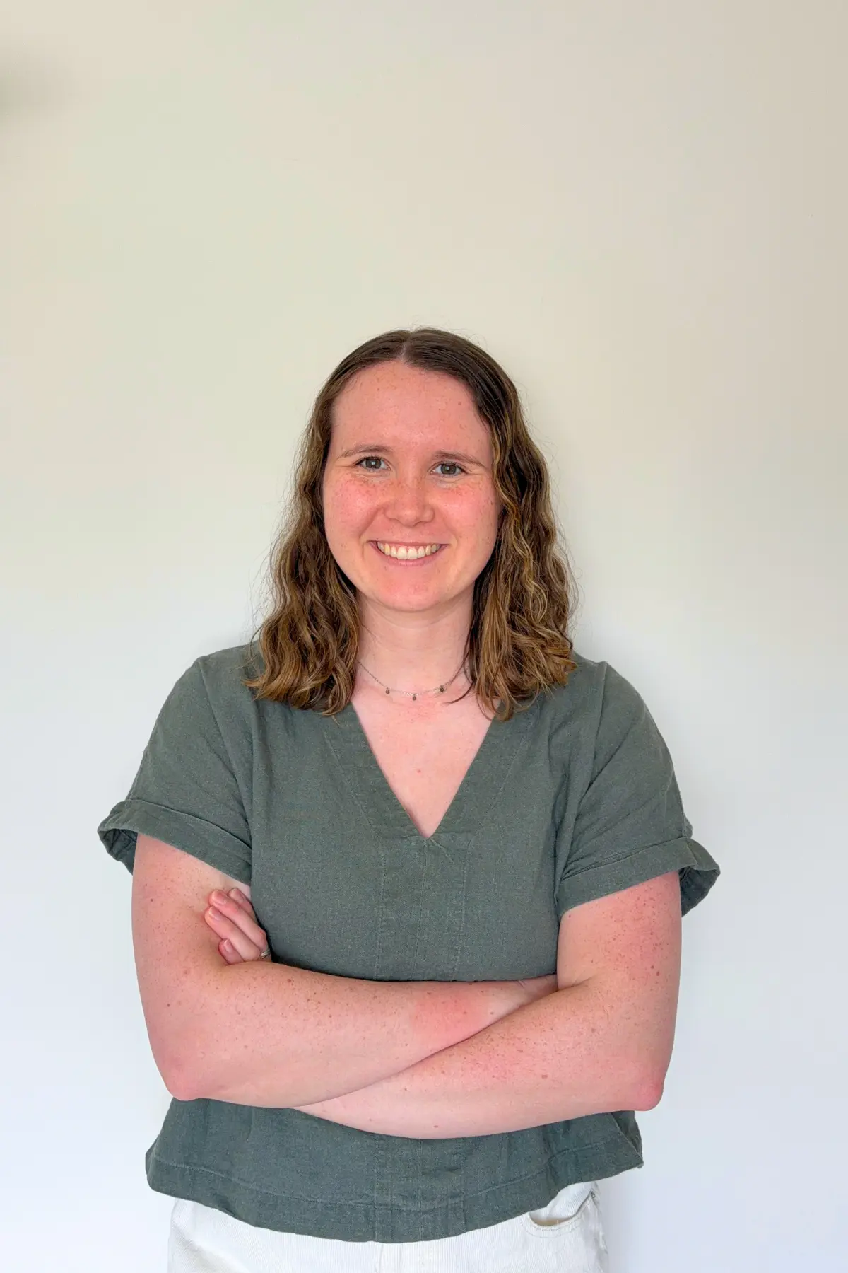 Olivia Laughman standing in front of a blank wall with her arms crossed